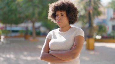 Parkta kollarını kavuşturmuş, ciddi ifadeleri olan Afro-Amerikalı genç bir kadın.