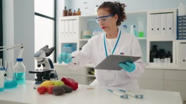 Middle age woman wearing scientist uniform write on clipboard at laboratory