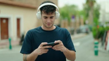 Young hispanic man smiling confident playing video game at street