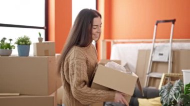 Young beautiful hispanic woman unpacking cardboard box at new home