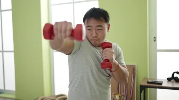若いです中国人男性使用ダンベルボクシングでスポーツセンター — ストック動画