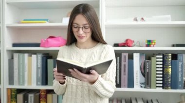 Young beautiful hispanic woman standing reading book at library university