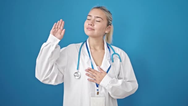 年轻美丽的惊慌失措的女医生 手托着胸膛在孤零零的蓝色背景下宣誓 — 图库视频影像