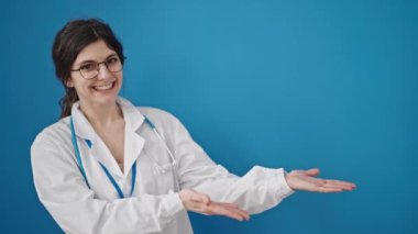 Genç, güzel İspanyol kadın doktor gülümsüyor kendine güvenen, izole edilmiş mavi arka planda sunan.