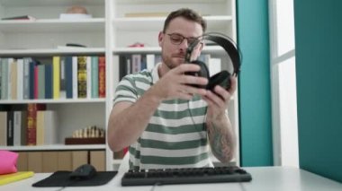 Young caucasian man using computer wearing headphones at library university