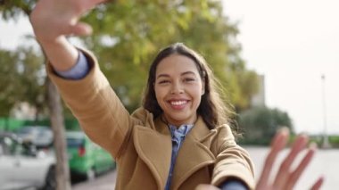 Genç, güzel, İspanyol bir kadın gülümsüyor. Parkta elleri ile çerçeve hareketi yapıyor.