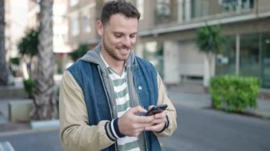 Young caucasian man smiling using smartphone at street