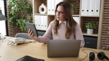 Young beautiful hispanic woman business worker using touchpad and laptop at office
