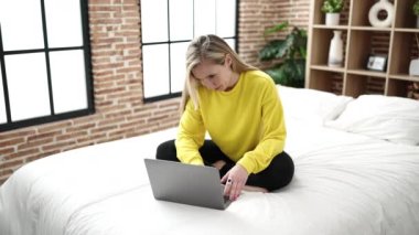 Yatak odasında dizüstü bilgisayar kullanan genç sarışın kadın.