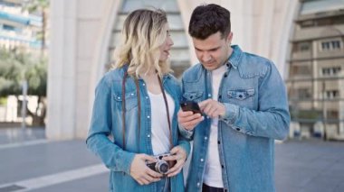 Kadın ve erkek caddede akıllı telefon kullanarak yan yana duruyorlar.