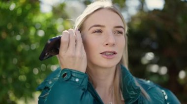 Young blonde woman listening to voice message at park