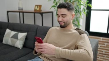 Young arab man using smartphone sitting on sofa at home