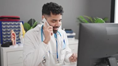 Genç İspanyol doktor, klinikte bilgisayarla akıllı telefondan konuşuyor.