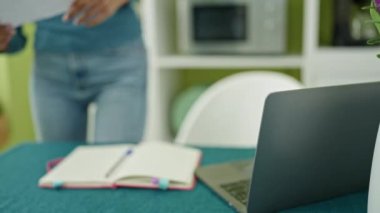 Young beautiful hispanic woman using laptop reading document at home