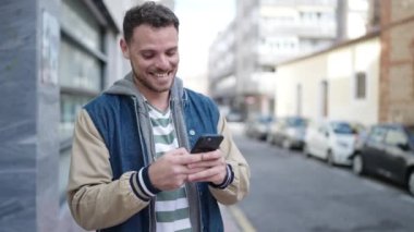 Young caucasian man smiling using smartphone at street