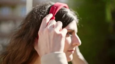 Young beautiful hispanic woman listening to music with serious expression at park