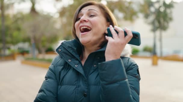 中年女性笑顔自信に満ちたリスニング音声メッセージによってスマートフォンによって公園 — ストック動画