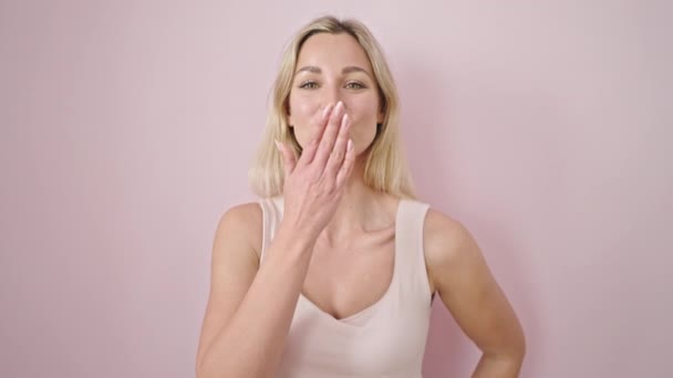 Молода Блондинка Посміхається Впевнено Дме Поцілунок Над Ізольованим Рожевим Тлом — стокове відео