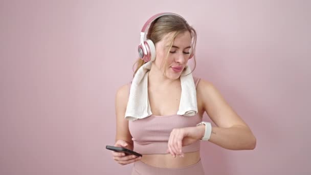 Mujer Rubia Joven Escuchando Música Mirando Cronómetro Sobre Fondo Rosa — Vídeo de stock