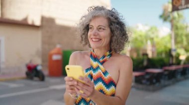 Middle age grey-haired woman smiling confident using smartphone at street