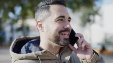 Genç İspanyol adam gülümsüyor. Parkta akıllı telefonla konuşuyor.