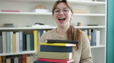 Kütüphane üniversitesinde elinde kitaplarla gülümseyen sarışın genç bir kız.