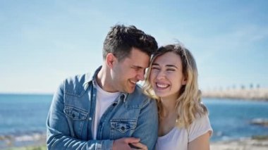 Kadın ve erkek gülümsüyor. Kendilerine güveniyorlar. Deniz kenarında sarılıyorlar.