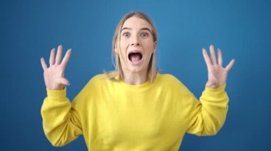 Sarışın genç bir kadın, ağzı kapalı, şaşırmış bir şekilde dikiliyor.