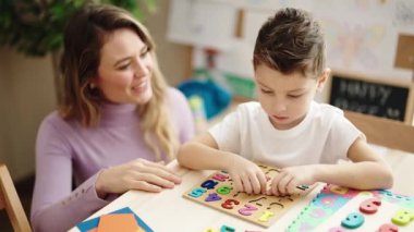 Anaokulunda masada oturan kadın ve çocuk matematik bulmaca oyunu oynuyorlar.