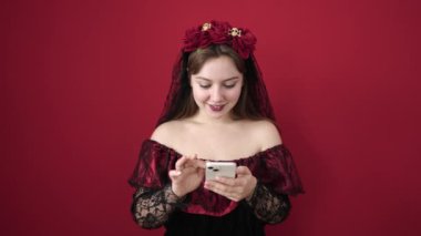 Katrina kostümü giyen genç sarışın kadın izole edilmiş kırmızı arka planda akıllı telefon kullanıyor.