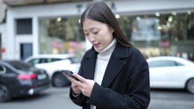 Sokakta akıllı telefon kullanan, kendine güvenen genç Çinli bir kadın.