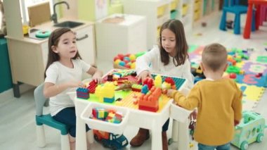 Anaokulundaki masada oturan bir grup çocuk inşaat bloklarıyla oynuyor.