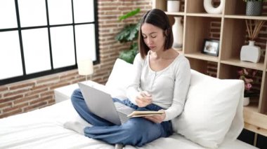 Yatak odasında dizüstü bilgisayar kullanan genç ve güzel bir İspanyol kadın.