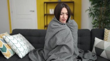 Young beautiful hispanic woman covering with blanket for cold at home