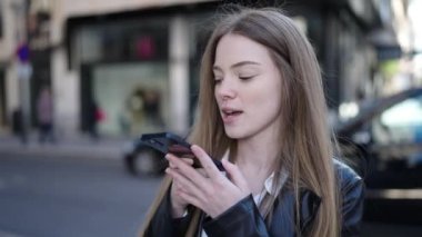 Young blonde woman sending voice message with smartphone at street