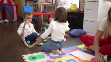 Kız ve oğlanlı öğretmen yere oturmuş kağıda resim çiziyor ve anaokulunda arabayla oynuyor.