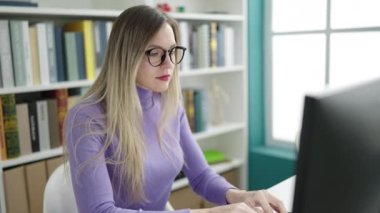 Young blonde woman student standing with i dont know expression at library university