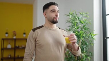 Genç Arap adam evde dikilip portakal suyu içiyor.