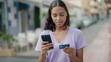 Young african american woman using smartphone and credit card at coffee shop terrace