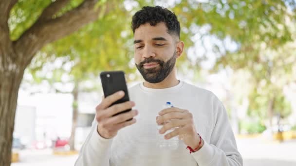 Joven Hispano Sosteniendo Botella Agua Usando Smartphone Parque — Vídeos de Stock