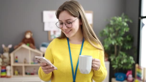 Young Blonde Woman Preschool Teacher Using Smartphone Drinking Coffee Kindergarten — Vídeo de Stock