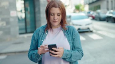 Young beautiful plus size woman smiling confident using smartphone at street