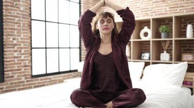 Young caucasian woman doing yoga exercise sitting on bed at bedroom