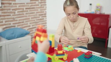 Sınıftaki masada oturan, inşaat bloklarıyla oynayan sevimli çocuk.