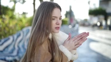 Young blonde woman blowing air on hands for cold at park