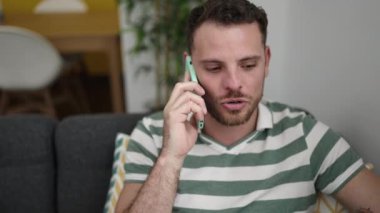 Young caucasian man speaking on the phone sitting on the sofa at home