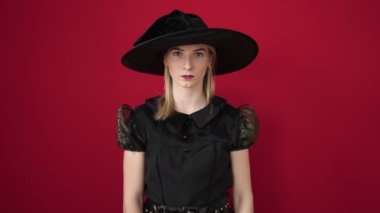 Young blonde woman wearing witch costume doing scare gesture over isolated red background