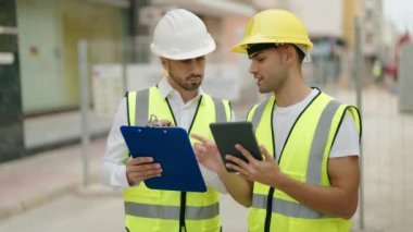 Two hispanic men architects reading document using touchpad at street