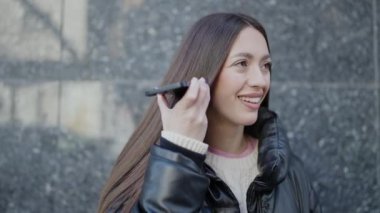 Genç ve güzel İspanyol kadın gülümsüyor. Caddedeki akıllı telefondan kendine güvenen bir sesli mesaj dinliyor.