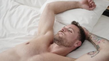 Young caucasian man waking up stretching arms at bedroom